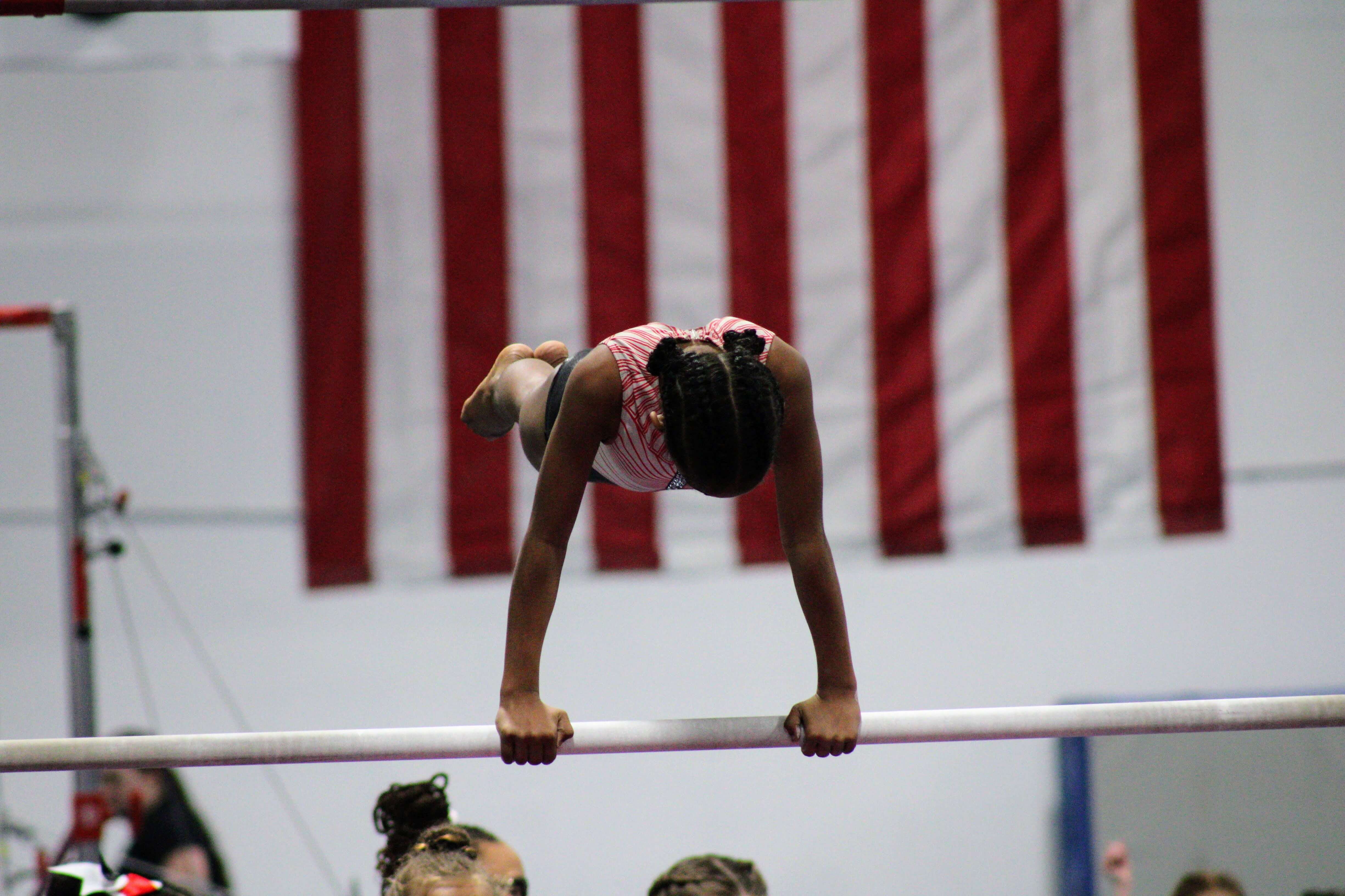 A gymnast on a bar with a flag in the background